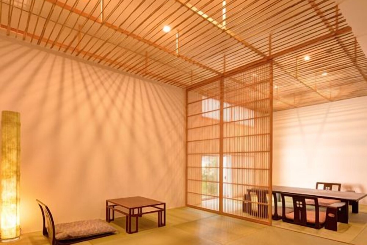Una habitación tradicional japonesa con suelo de tatami, una mesa baja con sillas y una puerta corredera.