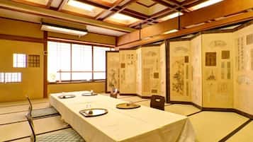 A traditional Japanese room with tatami flooring, a long table set for dining, and sliding doors with calligraphy.