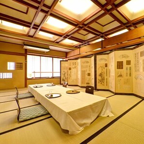 Una habitación japonesa tradicional con suelo de tatami, una mesa larga dispuesta para comer y puertas correderas con caligrafía.