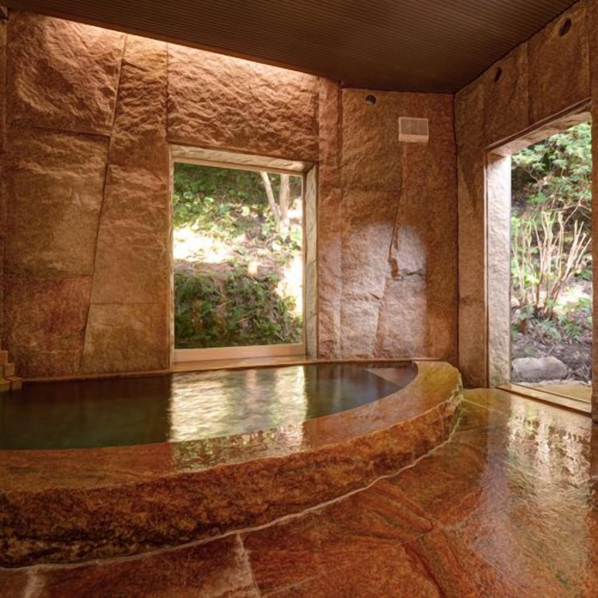 A stone-walled room with a hot tub and a window providing a view of greenery.