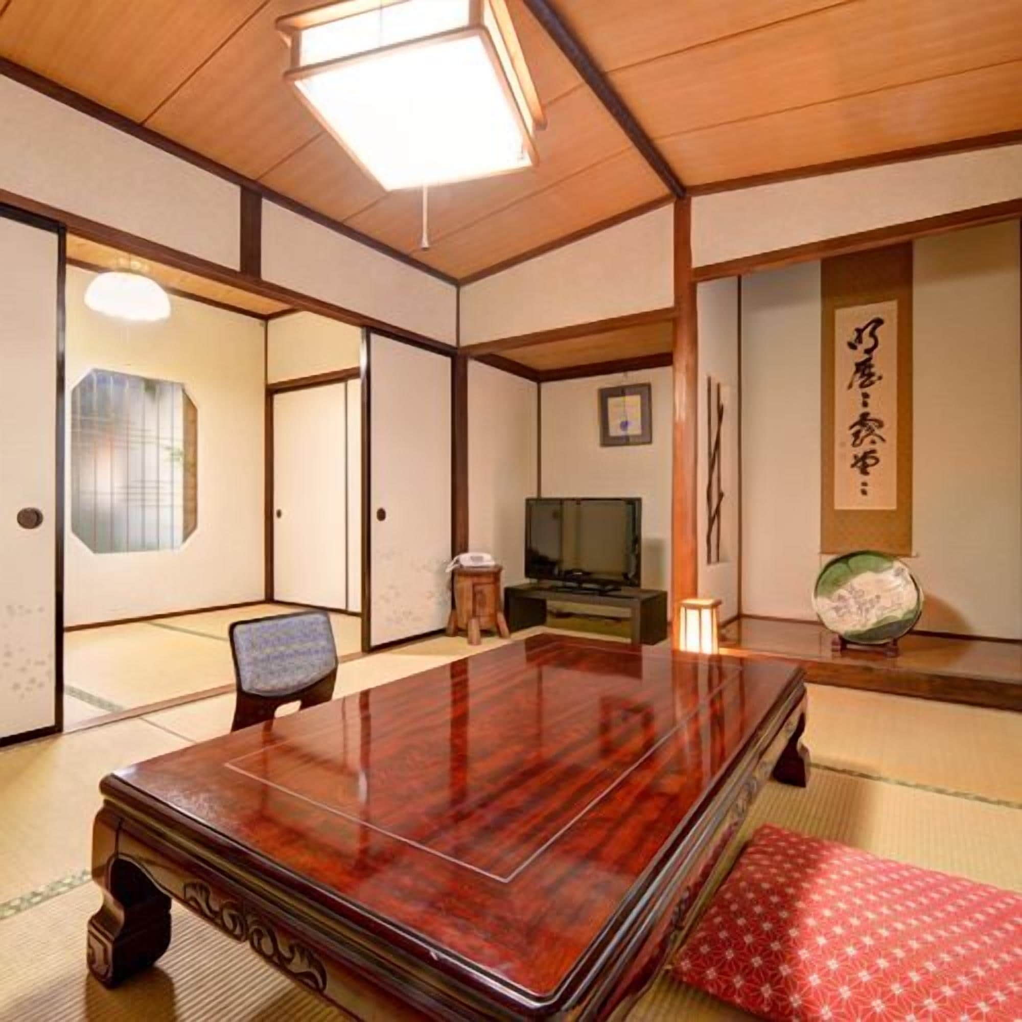 A traditional Japanese room with tatami flooring, a wooden table, a television, and a decorative item on the wall.