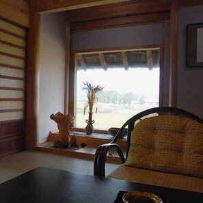 Una habitación con ventana, una silla, una mesa y un jarrón decorativo.