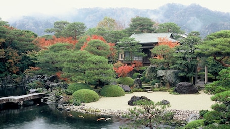A traditional Japanese garden with a pond, rocks, and a wooden building.