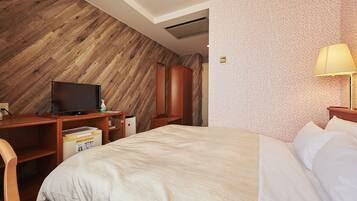 A hotel room with a wooden accent wall, a bed with white linens, a desk with a television, and a nightstand.
