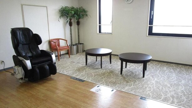 A room with a massage chair, two small tables, a potted plant, and a window. - Annex Royal Hotel (Odate)