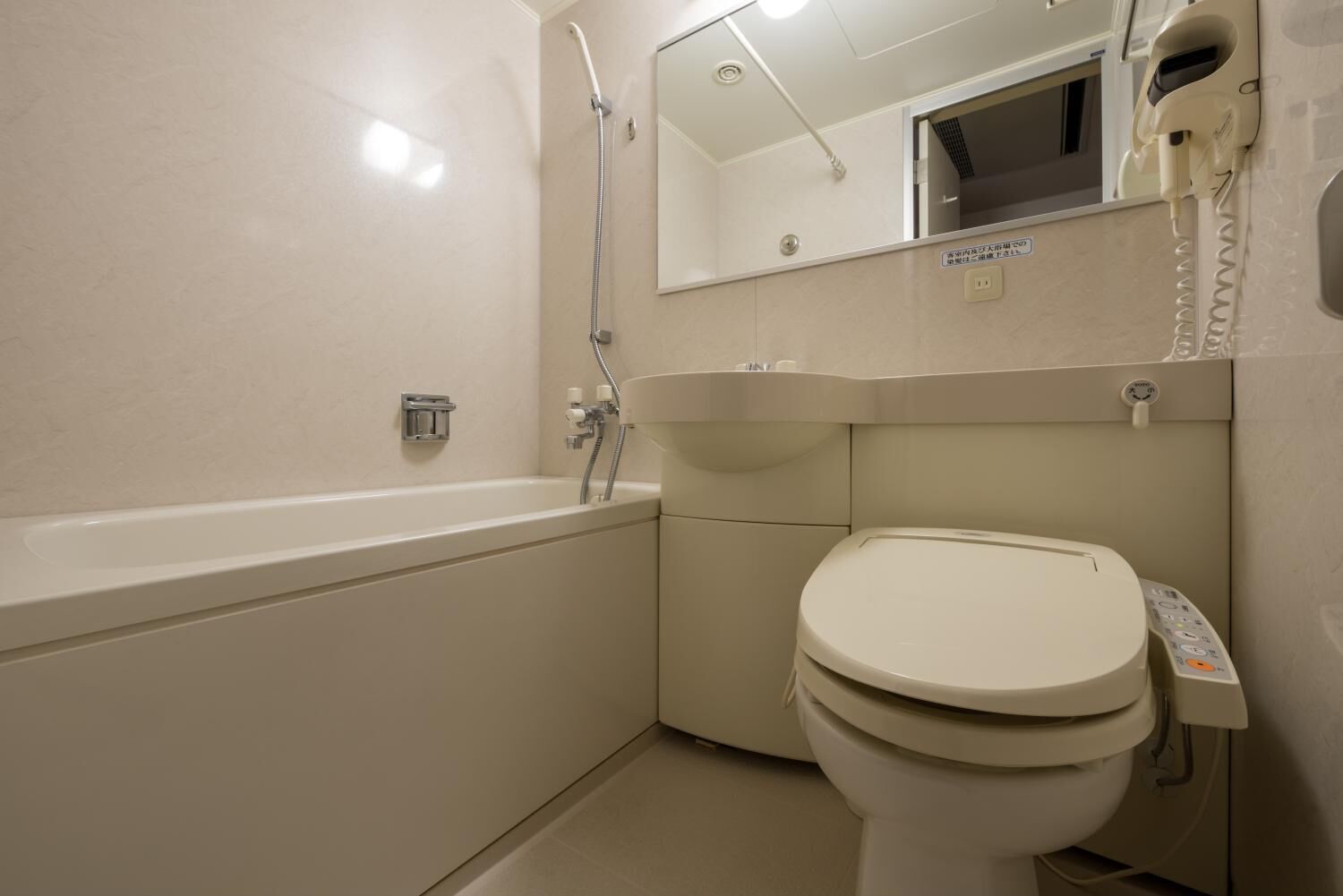 A small, modern bathroom with a bathtub, toilet, and a hand dryer.