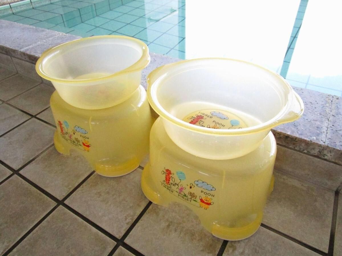 Två gula plastbehållare med tecknade figurer på, placerade på ett kaklat golv nära en pool.