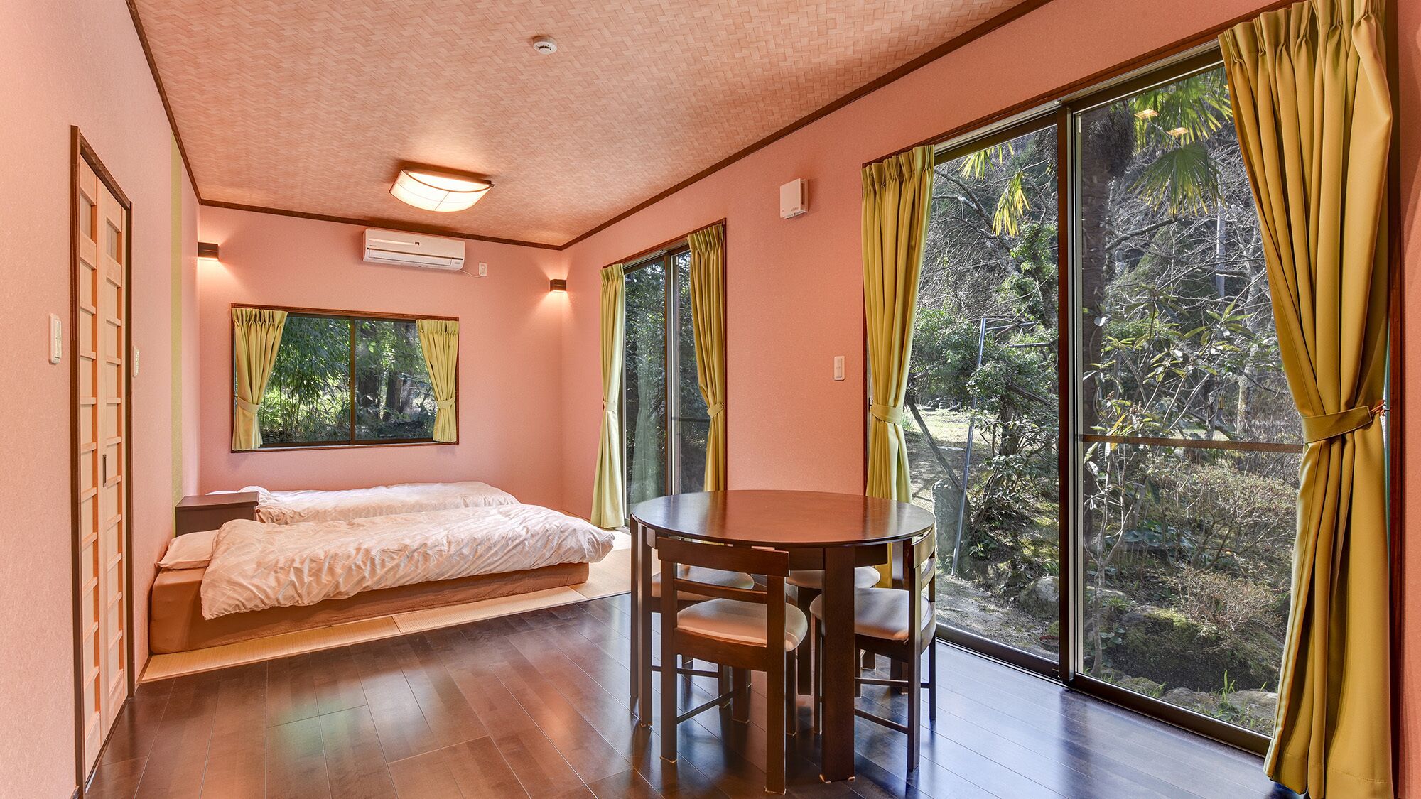 A bedroom with a bed, a table, chairs, and large windows with curtains.