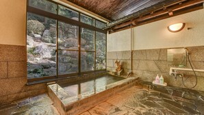 A bathroom with a large window, a stone bathtub, and a mirror.