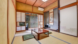 A traditional Japanese room with tatami flooring, a low wooden table, a TV, and sliding doors.