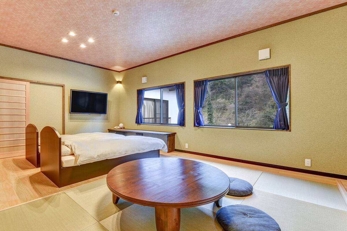 Une chambre avec un lit, un bureau, une télévision et une fenêtre avec des rideaux.