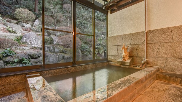 A hot spring bath with a view of rocky terrain and a statue.