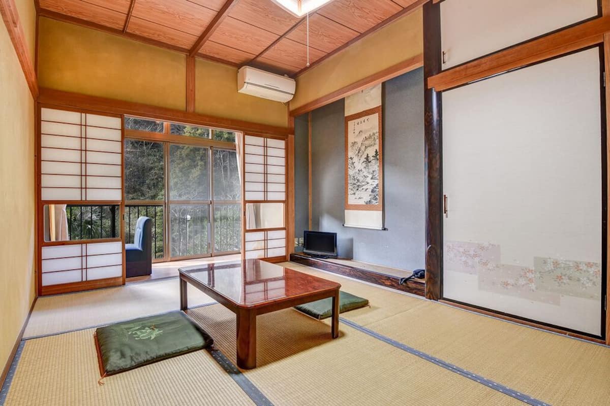 Une pièce de style japonais traditionnel, avec un sol recouvert de tatamis, une petite table en bois, des portes coulissantes et un téléviseur.