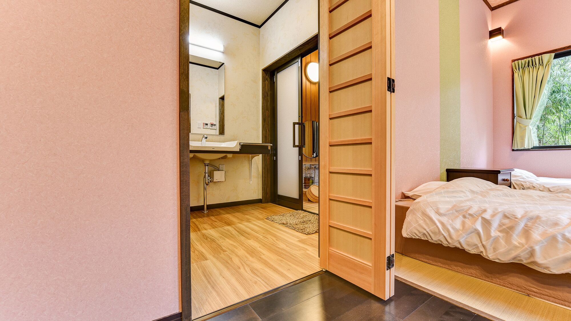 Une pièce dotée d’une porte coulissante en bois donnant sur une salle de bain, d’un lit avec une tête de lit et d’une fenêtre avec des rideaux.