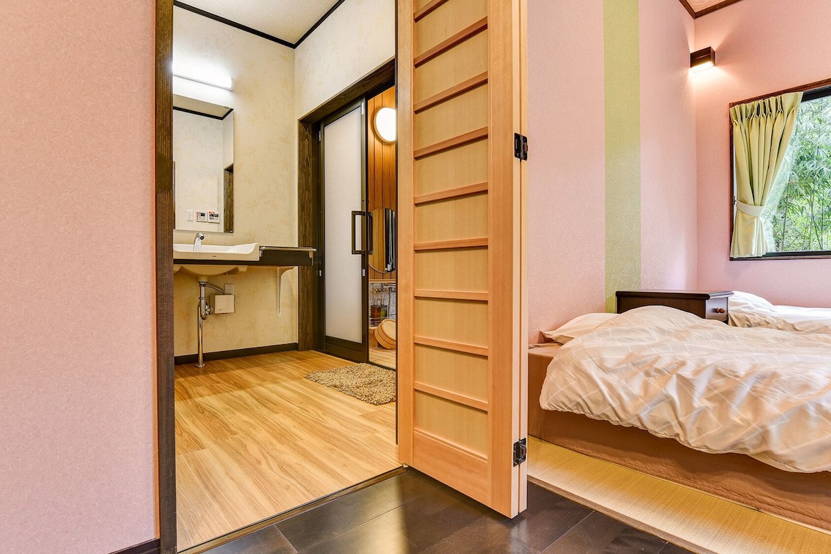 Une pièce dotée d’une porte coulissante en bois donnant sur une salle de bain, d’un lit avec une tête de lit et d’une fenêtre avec des rideaux.