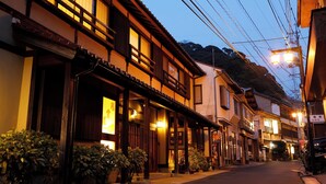 A traditional Japanese street at dusk with wooden buildings, illuminated signs, and power lines.
