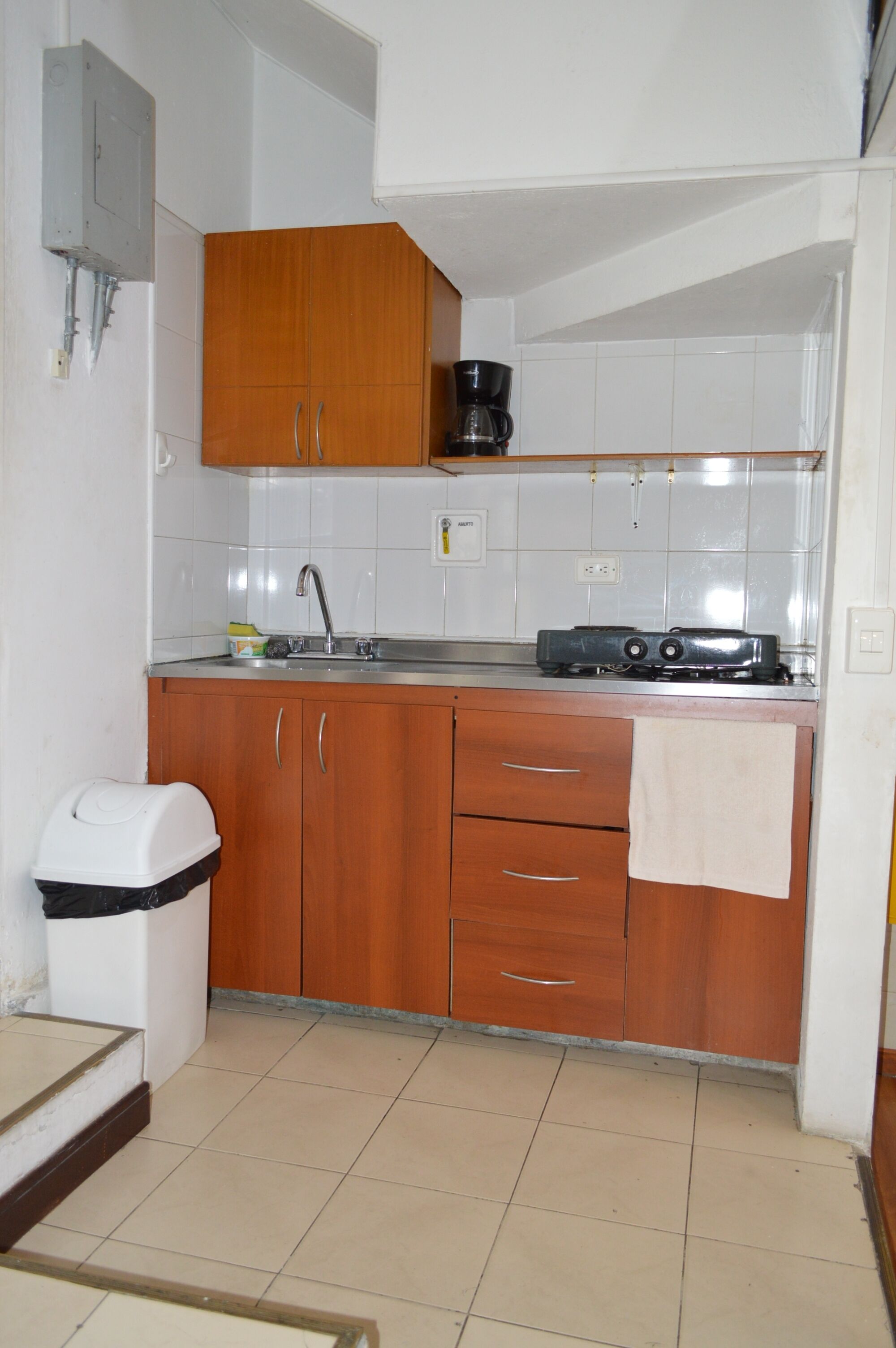 A compact kitchen with wooden cabinets, a sink, a stove, and a trash bin.