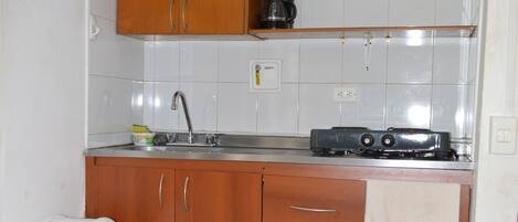 A compact kitchen with wooden cabinets, a sink, a stove, and a trash bin.