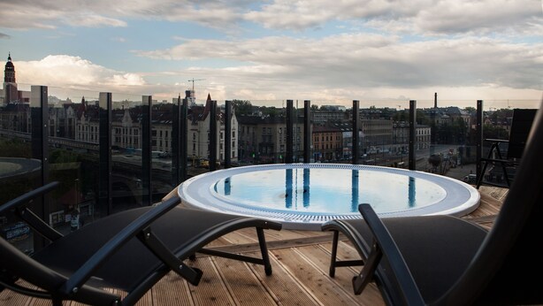 Ein Pool auf dem Dach mit Liegestühlen, der einen Blick auf eine Stadtlandschaft mit historischen Gebäuden und einer Brücke bietet.