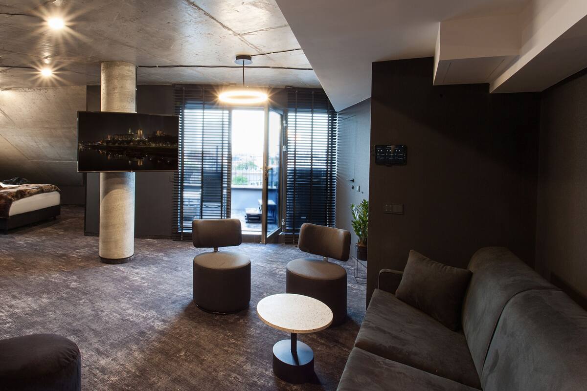 A modern lounge area with a large flat-screen TV, round seating, and a view of the city through large windows.