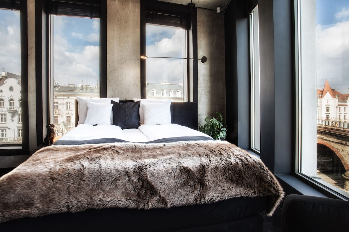 A bed with a fur throw, a view of a bridge, and a cityscape through large windows.