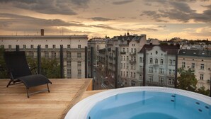 Eine Dachterrasse mit Whirlpool, Liegestuhl und Blick auf historische Gebäude.