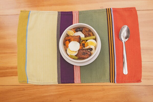 A bowl of food on a table with a spoon and a colorful placemat.