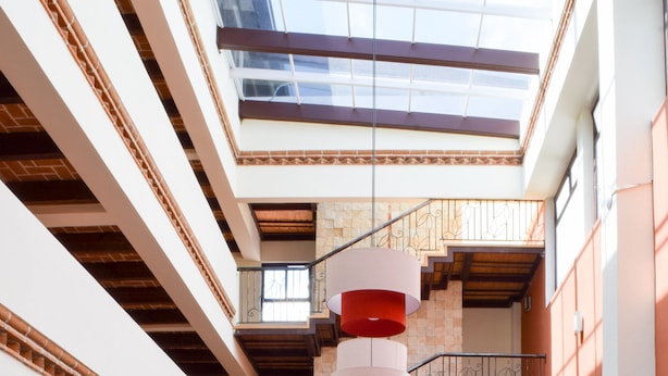 A spacious atrium with a central staircase, red seating, and a high ceiling with skylights. - Plaza Magnolias Suites (San Cristóbal de las Casas)