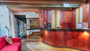 A hotel lobby with a reception desk, a red sofa, and a staircase leading to another floor. - Plaza Magnolias Suites (San Cristóbal de las Casas)