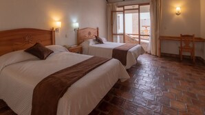 A room with two beds, a wooden headboard, a brick floor, and a balcony with a table and chair. - Plaza Magnolias Suites (San Cristóbal de las Casas)