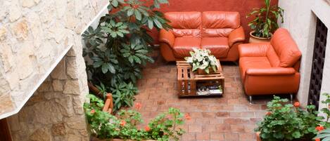 Une cour bordée de murs en pierre, avec des murs rouges, deux canapés en cuir et des plantes en pot.