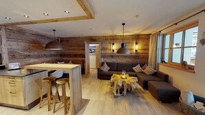 A modern interior with a wooden accent wall, a central island with stools, a sofa with patterned cushions, and a rustic coffee table. - The Peak Hochkönig (Dienten am Hochkoenig)