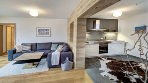 A modern living room with a sofa, a coffee table, and a kitchen area with a stove and cabinets. - The Peak Hochkönig (Dienten am Hochkoenig)