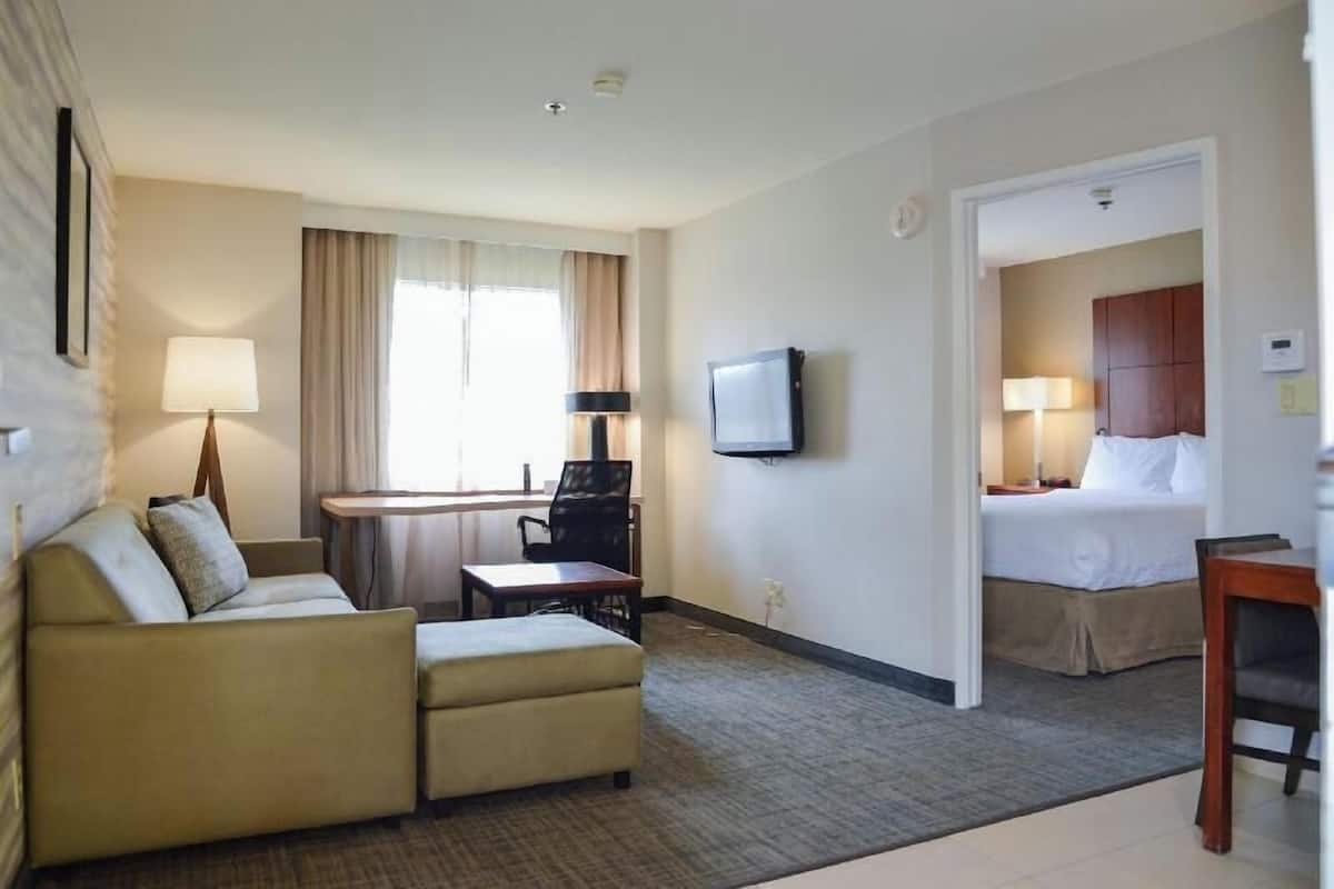 Une chambre d’hôtel équipée d’un canapé, d’un bureau, d’une télévision, d’un lit et d’une porte donnant sur une autre pièce.