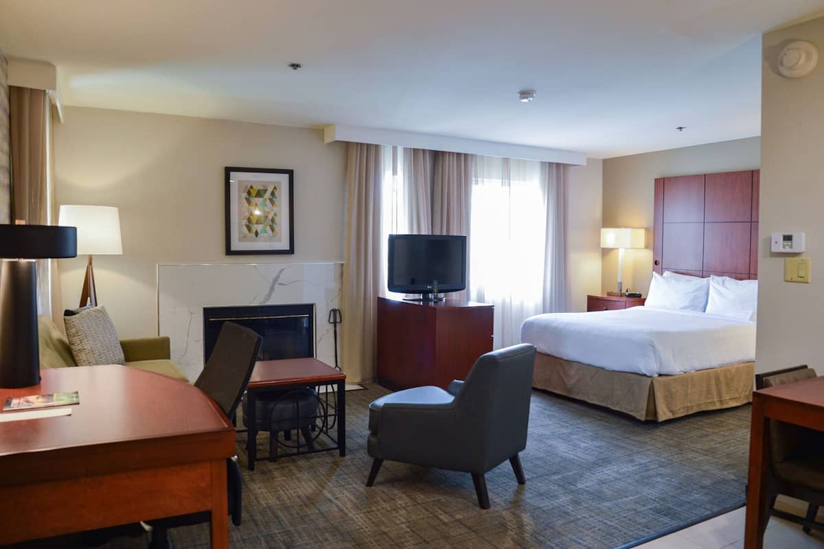 Une chambre d’hôtel équipée d’un lit, d’un bureau, d’une chaise, d’une télévision, d’une cheminée et d’une fenêtre avec des rideaux.