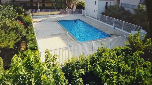 Une piscine rectangulaire entourée d’une clôture blanche, avec en arrière-plan des immeubles résidentiels et de la verdure.