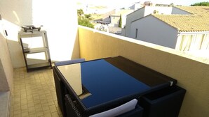 Un petit balcon avec une table à plateau en verre et deux chaises en osier.