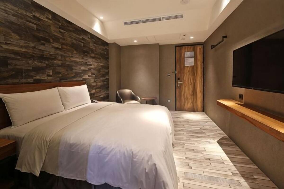 Hotellihuone, jossa on suuri sänky, puinen pääty, televisio, pieni pöytä ja ovi.