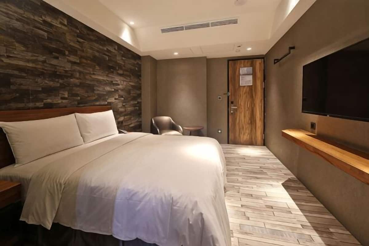 A hotel room with a large bed, a wooden headboard, a television, a small table, and a door.