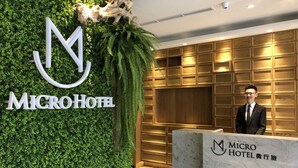 A reception desk with a logo and name "MICRO HOTEL" on the wall behind it. - Micro Hotel (Taichung)