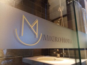 A bathroom with a sink and a mirror. The wall has a sign that reads "MICRO HOTEL". - Micro Hotel (Taichung)