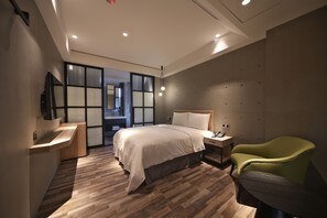 A modern hotel room with a wooden floor, a bed with white bedding, a green armchair, a bedside table, and a TV mounted on the wall. - Micro Hotel (Taichung)