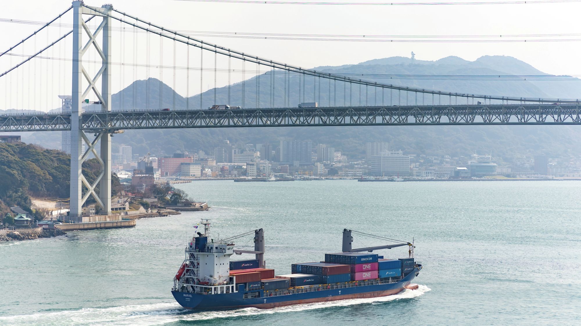 Ein Frachtschiff mit zahlreichen Containern fährt unter einer großen Hängebrücke.