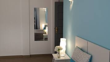 Un dormitorio con cama, mesita de noche, lámpara y espejo.