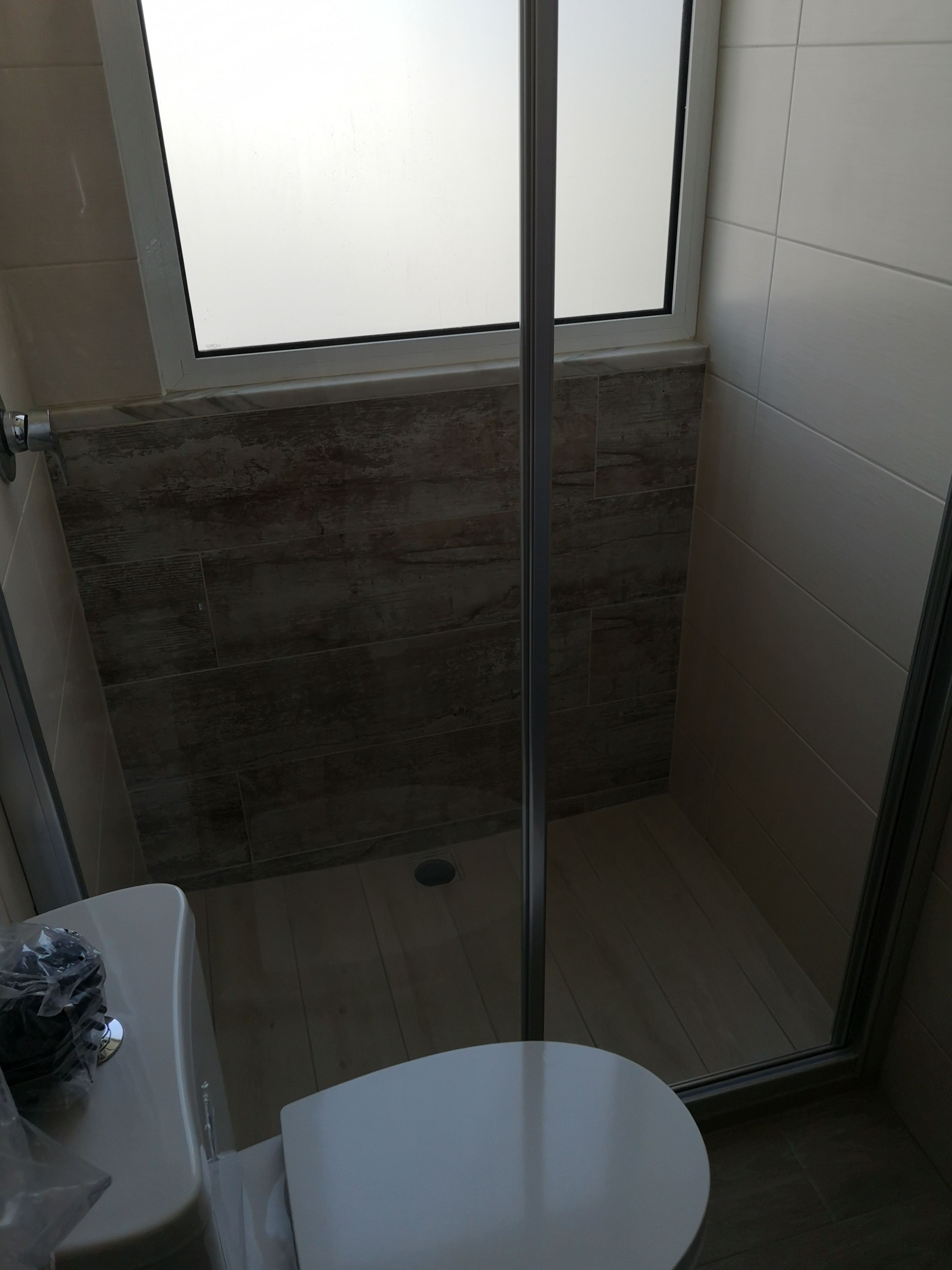 A small, enclosed shower area with a glass door, a toilet, and a window above the shower.