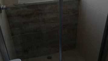 A small, enclosed shower area with a glass door, a toilet, and a window above the shower.