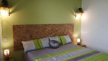 A bedroom with a wooden headboard, a bed with green and gray bedding, bedside lamps, and an air conditioner on the wall.