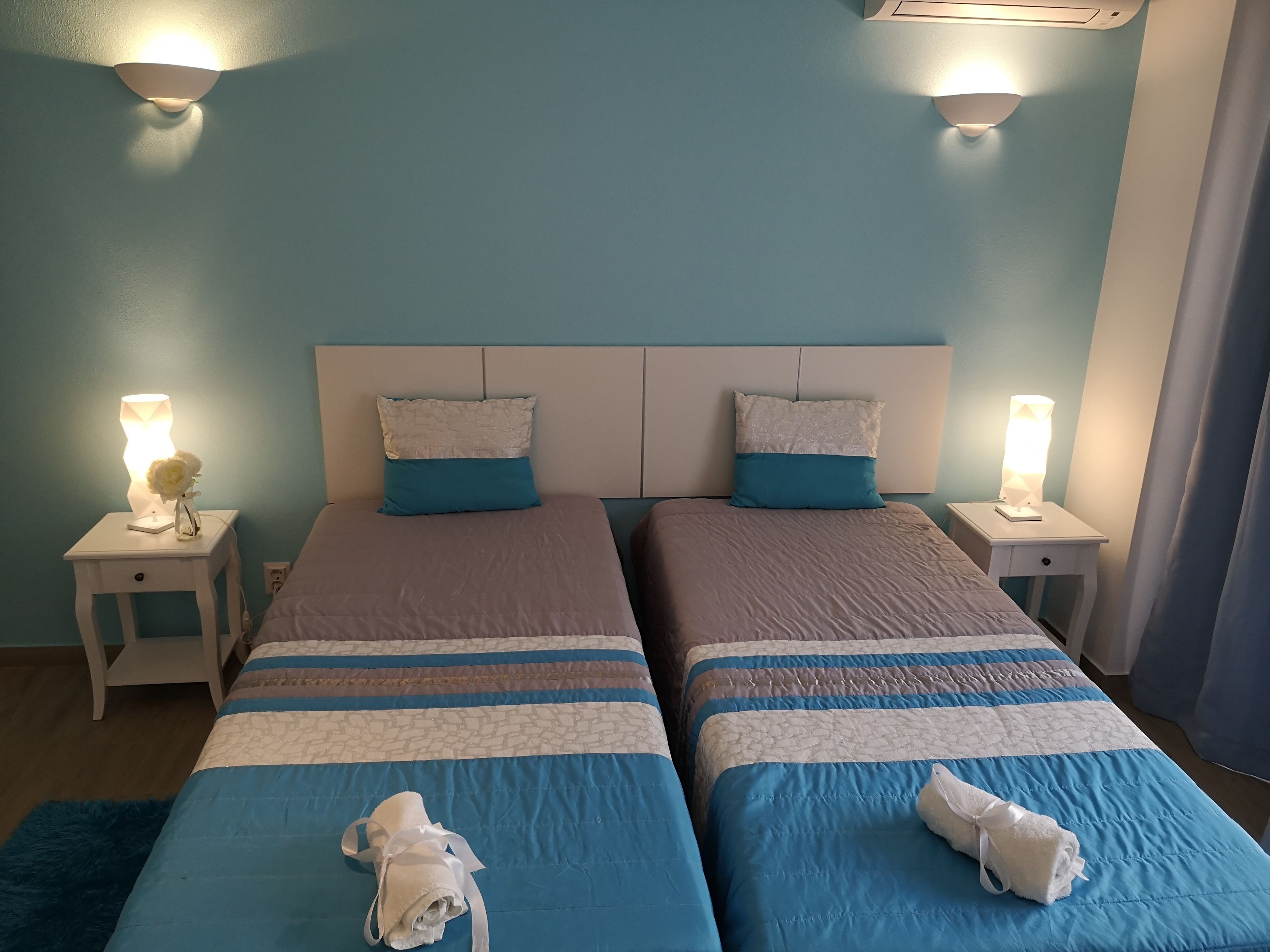 A double room with two beds, each with a headboard, bedside tables, and lamps. There are towels on the beds.