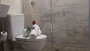Un baño con inodoro, mampara de ducha de vidrio y lavamanos con toalla y una rosa sobre el inodoro.