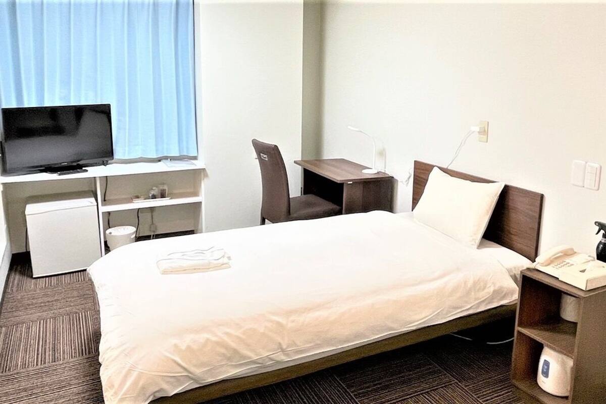 Une chambre d’hôtel équipée d’un lit, d’un bureau, d’une chaise, d’une télévision et d’une petite kitchenette.